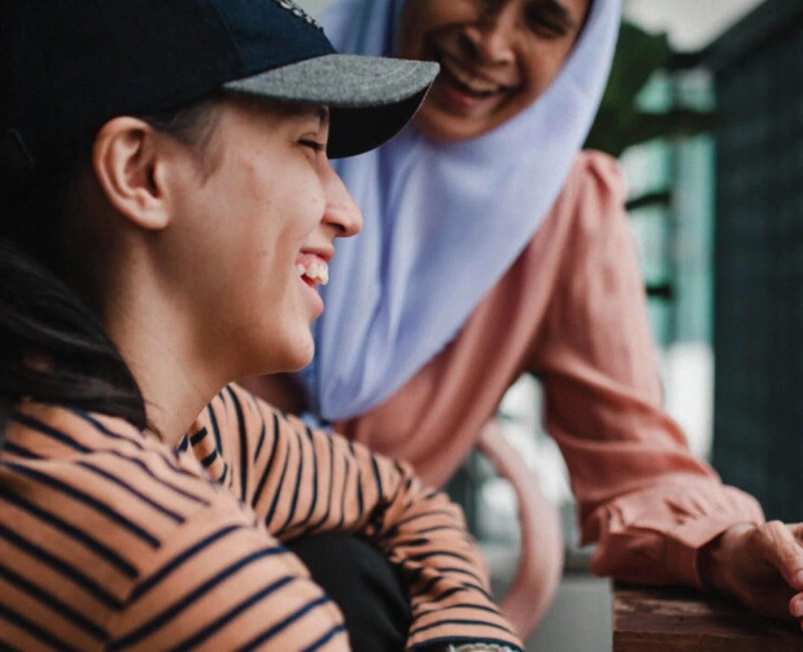 Two women smiling and talking together, one wearing a cap and the other a headscarf. (photo)