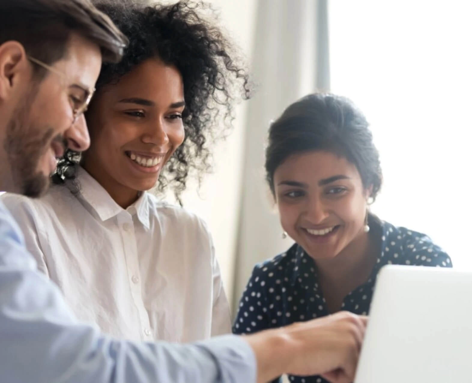 Three colleagues looking at a laptop screen and smiling while working together. (photo)