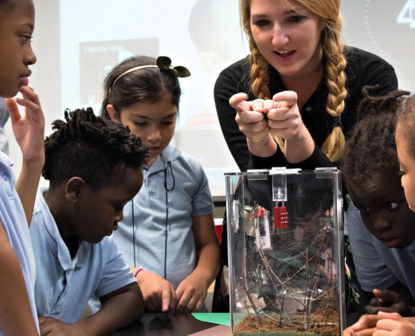 A teacher showing a small object to a group of young students in a classroom. (photo)