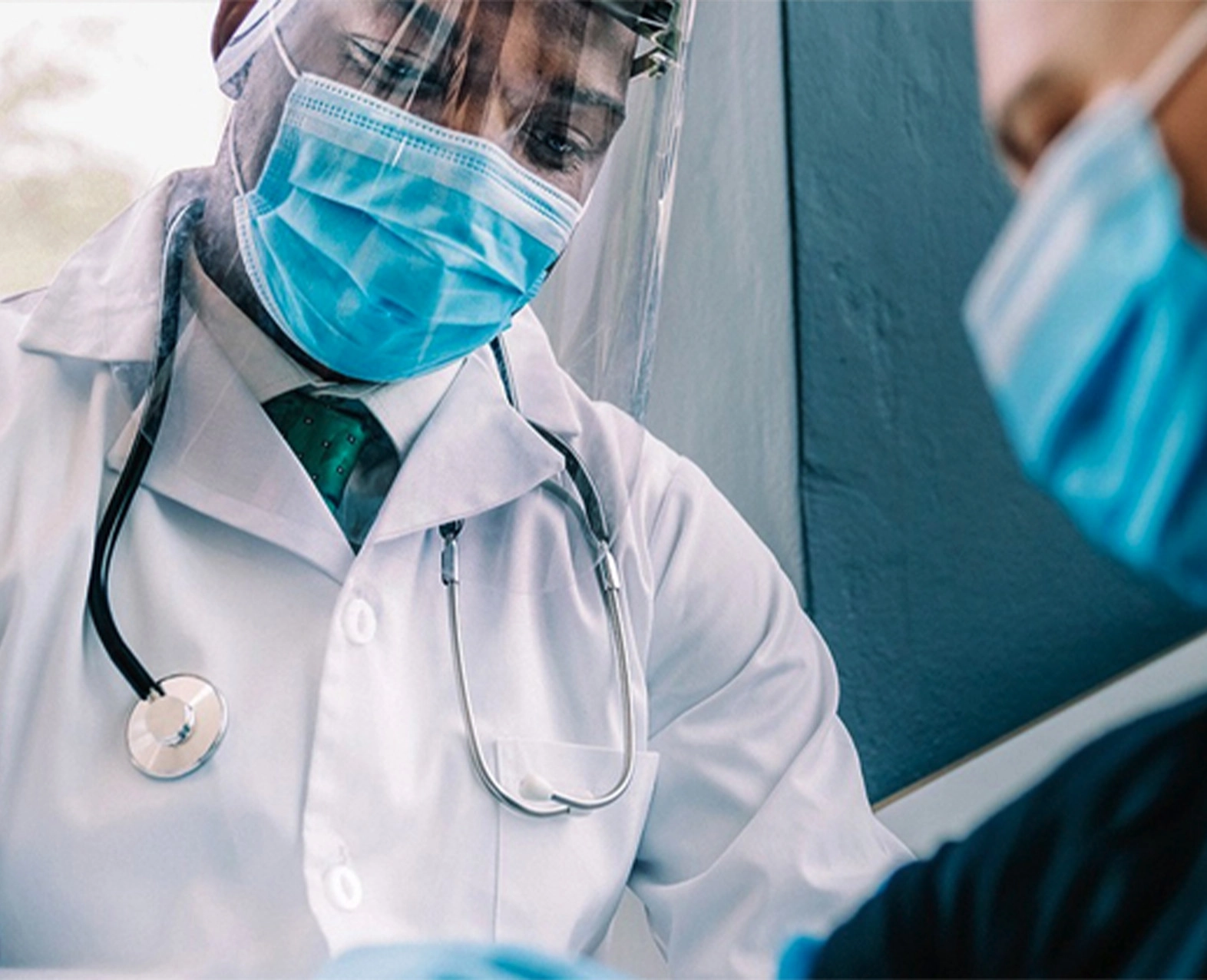 A healthcare worker in a mask and face shield attending to a patient. (photo)