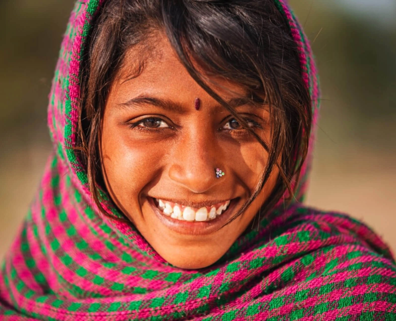 A close-up of a smiling girl wearing a colorful scarf with a bindi on her forehead. (photo)