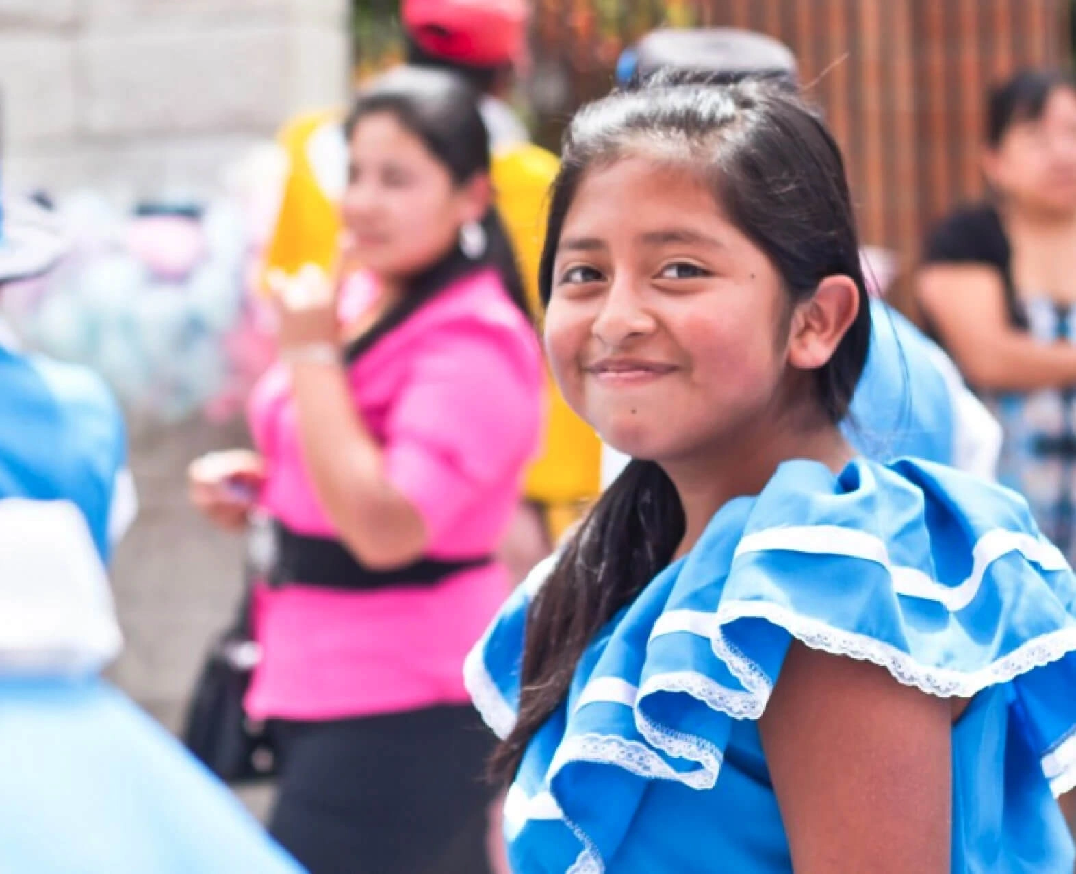 A young girl smiling during a community event with other people in the background. (photo)