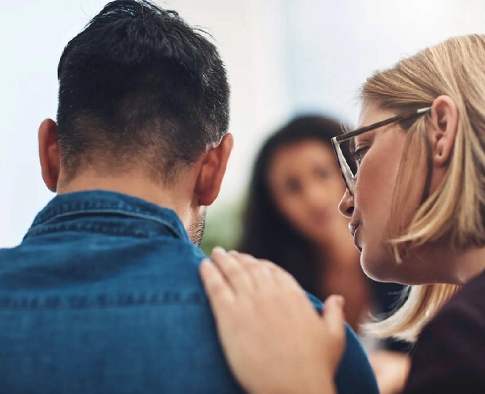 A woman comforting a man by placing a hand on his shoulder. (photo)